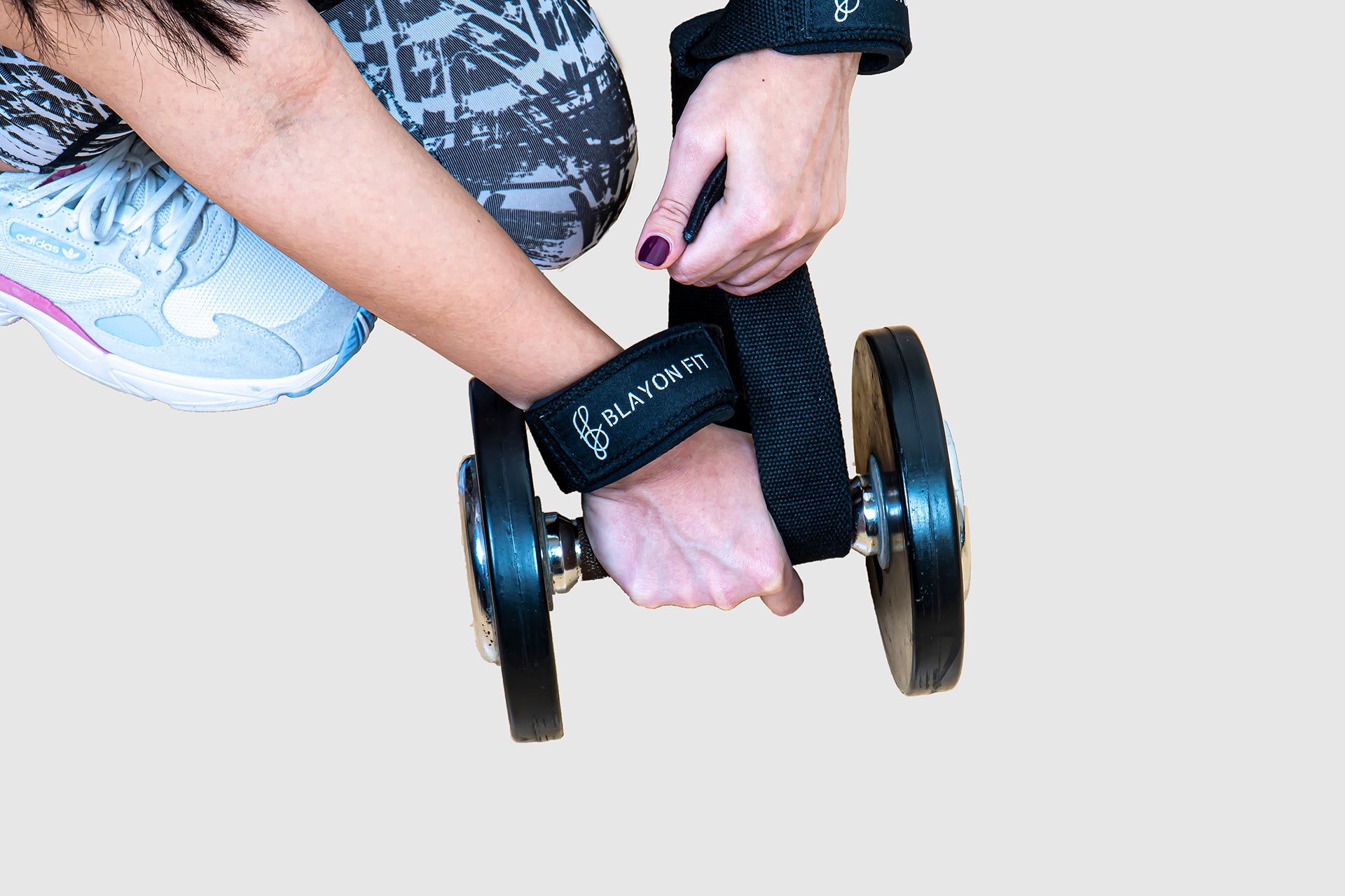 woman using the wrist strap to secure her grip while performing a dumbbell row exercise. 